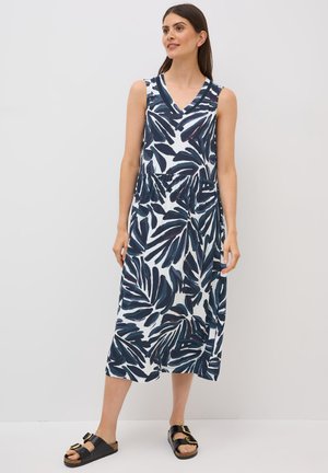 Long, sleeveless dress featuring a navy and white leaf pattern, v-neck design, gathered waist, and a loose fit. Paired with black slide sandals.