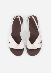 Paire de sandales avec semelles marron, larges brides croisées écru et brides arrière à lanières sur un fond uni.