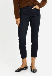 Pantalones azul marino con un diseño entallado, textura suave y longitud recortada. Combinados con zapatos planos negros adornados con tachuelas plateadas.