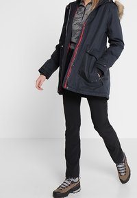 Mörk marinblå parka med pälskantad huva, dragkedjeförslutning och sidofickor. Kombinationen med svarta byxor och bruna vandringsskor med grå snören.