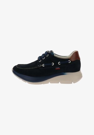 Zapato casual de ante azul marino con suela blanca, lengüeta marrón en el talón, cierre de cordones en la parte delantera y detalle de costura lateral.