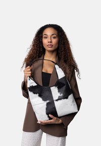 Svart och vit kohudsväska med jämn yta, halvmåneformad handtag och kontrasterande lapptäckesdesign.