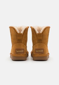 Bottines en suède marron avec doublure en fourrure douce, semelle en caoutchouc plate et une languette à l'arrière. Présente un logo brodé sur le côté.