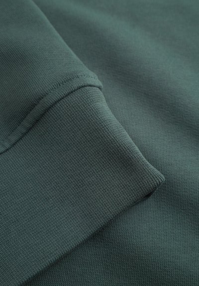 Tissu de sweat-shirt vert foncé, présentant une texture côtelée et un gros plan du détail de la manche, mettant en valeur un tissage lisse et uniforme.