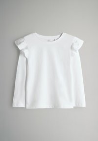 Vit långärmad t-shirt i bomull, med volangdetaljer på axlarna, rundad halsringning och rak fåll.