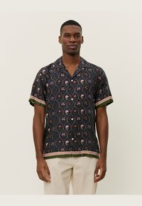 Short-sleeved shirt in dark fabric with floral pattern in pink, green, and orange. Features a contrasting green hem and striped accents.
