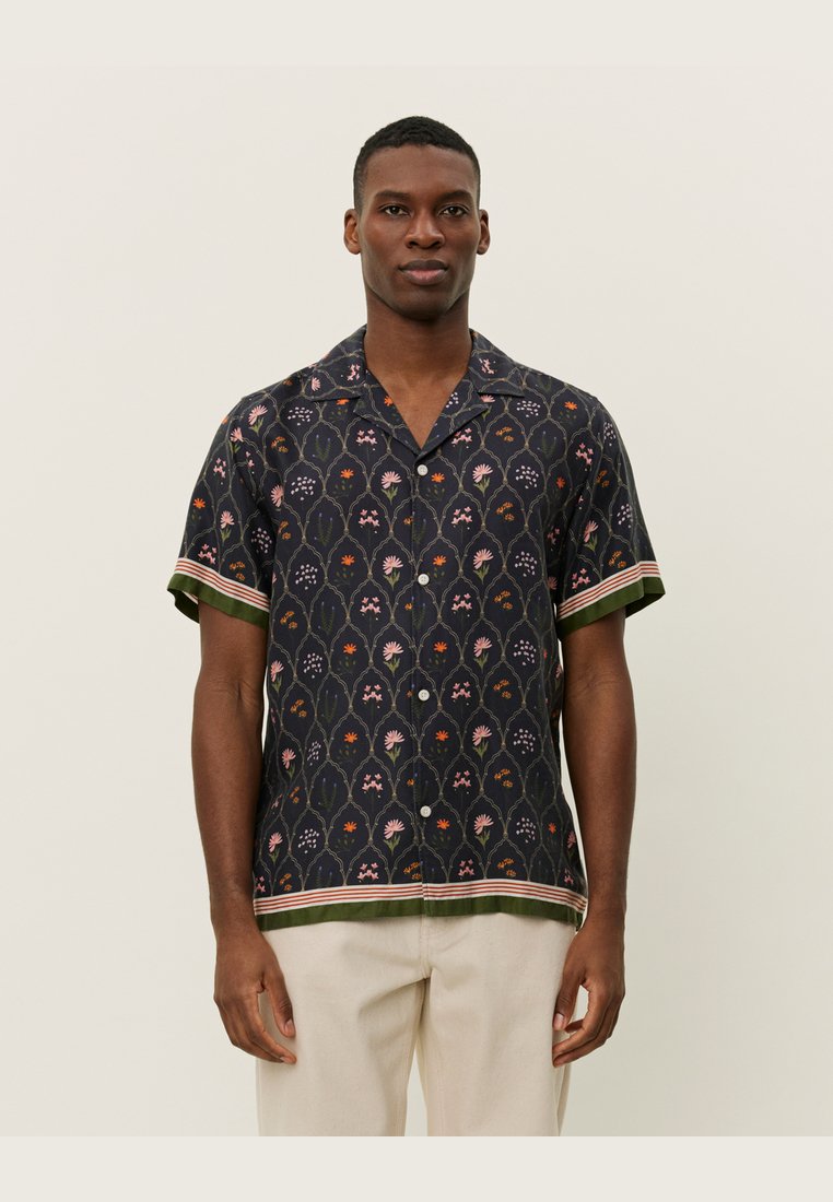 Short-sleeved shirt in dark fabric with floral pattern in pink, green, and orange. Features a contrasting green hem and striped accents.