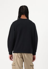 Černá mikina s kulatým výstřihem a raglánovými rukávy, se žebrovanými manžetami a lemem, vyrobená z měkké, texturované látky.