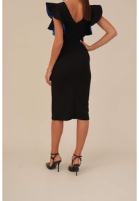 Robe ajustée noire avec des manches à volants bleues, décolleté en V dans le dos et ourlet mi-genou. Associée à des sandales à talons hauts noires à lanières.