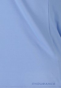 Vaaleansininen urheilupaita, joka on valmistettu sileästä kankaasta ja jossa on pyöreä kaula-aukko, lyhyet hihat ja "ENDURANCE" -printti helman lähellä.