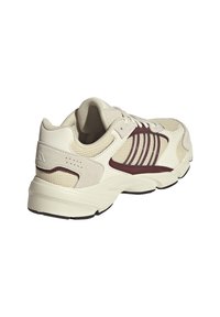 Weißer Sportschuh mit einem Obermaterial aus Mesh, kastanienbraunen Streifen als Akzent, strukturierten beigen Überzügen und einer gepolsterten Sohle mit markantem Design.