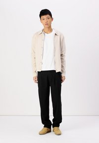 Light beige cardigan, white t-shirt, black trousers, and tan sneakers. Cardigan features buttons and a soft texture. Plain design, relaxed fit.