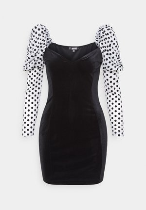 Robe bodycon en velours noir avec manches longues bouffantes blanches présentant de gros pois noirs et un décolleté carré.