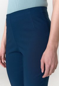 Marineblauwe, op maat gemaakte broek van stretchstof. Heeft een slim fit, een gladde textuur en een discreet zijzakje.
