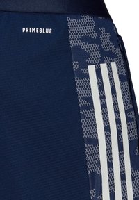 Tela azul oscuro con patrón de panal, rayas verticales blancas, texto "PRIMEBLUE" y una cremallera en el lado derecho.