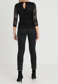 Black lace top with three-quarter sleeves, featuring a keyhole back opening, paired with fitted black jeans and ankle boots.
