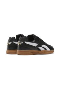 Sapatilhas de couro preto com detalhes brancos, apresentando uma sola de borracha de goma e um colarinho acolchoado. Logótipo da Reebok no calcanhar e listras laterais.