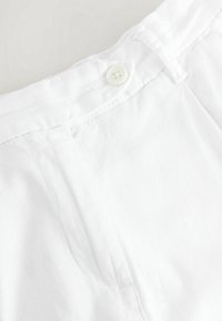 Hosenbund aus weißem Leinen mit einem einzelnen runden Knopf, flache Vorderseite mit leichtem Faltenwurf und sichtbaren Nähdetails.