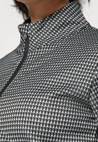 Black and white patterned zip-up sports top with a high collar, featuring a smooth texture and reflective accents.