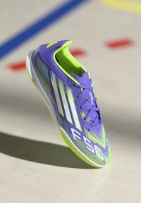 Paarse en groene sportschoen met een textuur en een lichtgewicht ontwerp, met opvallende witte strepen en "F50" branding aan de zijkant.