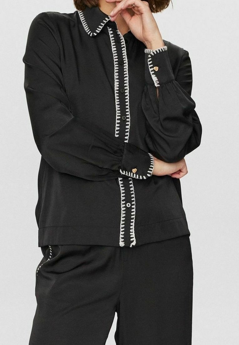 Black blouse with long sleeves, button front, and white stitching accents. Features balloon sleeves and heart-shaped button details.