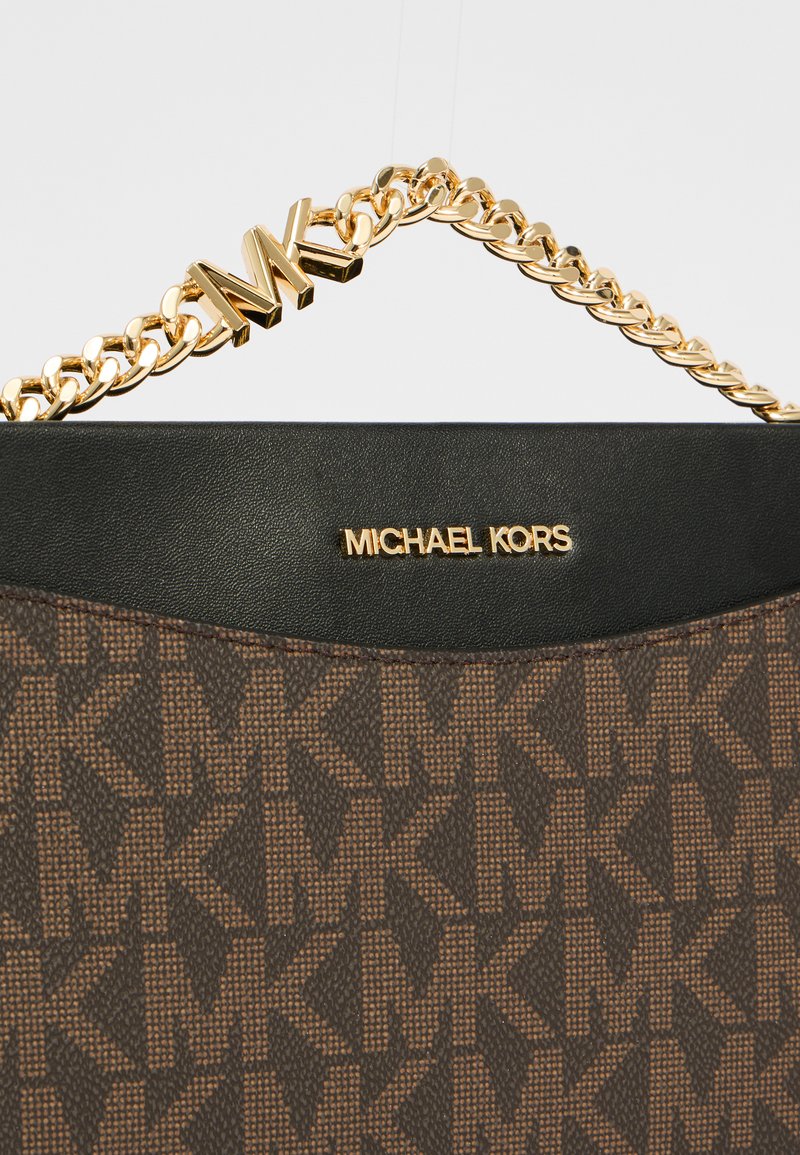 Bruine tote bag met een getextureerd MK-logo patroon, zwarte leren accenten, gouden kettingband en gouden "MICHAEL KORS" branding aan de voorkant.