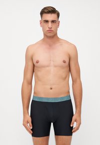 Čierne pánske boxerky s jemne modrým elastickým pásom s textom "UNDER ARMOUR". Hladká tkanina, priliehavý strih, dĺžka do polovice stehna.
