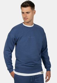 Felpa blu in cotone, con scollatura tonda, polsini e orlo a costine, arricchita da un discreto logo ricamato sul petto e sulla manica.