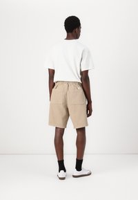 Beige fløjspidse shorts med elastisk liv og to baglommer, parret med en hvid t-shirt og sorte ankelstrømper.