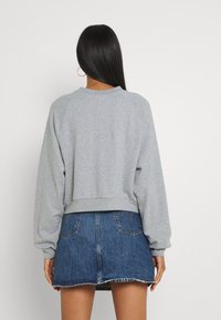 Sweatshirt gris court à manches longues, avec des poignets et un ourlet côtelés, associé à une mini-jupe en denim avec un bord effiloché et des poches à l'arrière.