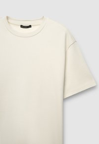 Maglietta a maniche corte color crema realizzata in morbido cotone, caratterizzata da una scollatura rotonda e una vestibilità rilassata. Design minimalista senza motivi.