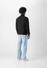 Black zip-up sweatshirt with high collar, paired with light blue loose-fitting jeans and white sneakers, shown from the back.