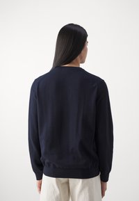 Pull en tricot bleu marine avec un col rond, des poignets et une ceinture côtelés, présentant une texture lisse et un design simple.