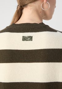 Randig tröja i mörkgrön och gräddfärgad med växlande färger. Har en rundad halsringning och inbäddad logotyp på baksidan, mjuk textur.