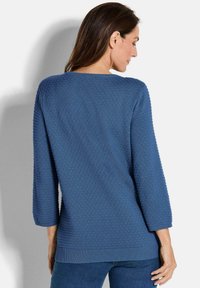 Blauer strukturierter Pullover mit Dreiviertelärmel und Rundhalsausschnitt. Weicher Stoff mit einem Muster aus erhabenen Punkten. Direkt im Rücken geschnitten.