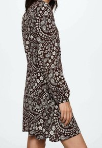 Braunes, floral gemustertes Kleid mit langen Ärmeln und enganliegendem Mieder, das einen weit ausgestellten Rock hat. Der Stoff ist leicht und strukturiert.