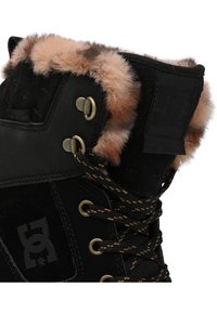 Bota negra elegante con bordes de piel sintética, ojales dorados y cordones negros. Presenta un material duradero y etiqueta de impermeabilidad.