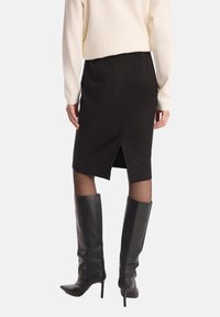 Czarna, prążkowana spódnica ołówkowa z tylnym rozcięciem, zestawiona z czarnymi, wysokimi butami na obcasie. Góra to kremowy sweter z długim rękawem.