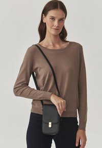 Maglione marrone a maniche lunghe con orlo a coste, abbinato a una borsa a tracolla in pelle nera con chiusura in oro e texture liscia.