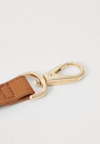 Cinturino in pelle marrone con un gancio in metallo dorato. Il gancio presenta un gancio funzionale ed è inciso con la scritta "VALENTINO". Texture liscia.