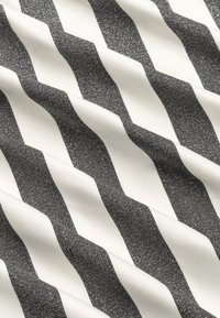 Textilie s vzorem šípov v černé a bílé barvě, s protichůdnými pruhy vytvářejícími texturovaný, vlnitý vzhled.
