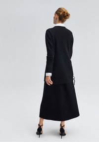 Maglione nero a maglia con maniche lunghe, caratterizzato da un collo rotondo e un look stratificato sopra una camicia bianca con colletto, abbinato a una gonna maxi nera.