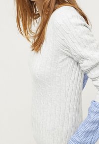 Maglione grigio a maglia con un motivo testurizzato e maniche lunghe; presenta polsini a fantasia blu su entrambi i lati.