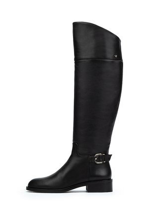 Bota de cuero negro hasta la rodilla con textura suave, punta redondeada, tacón bajo y detalle de hebilla lateral. Diseño único del eje alto.