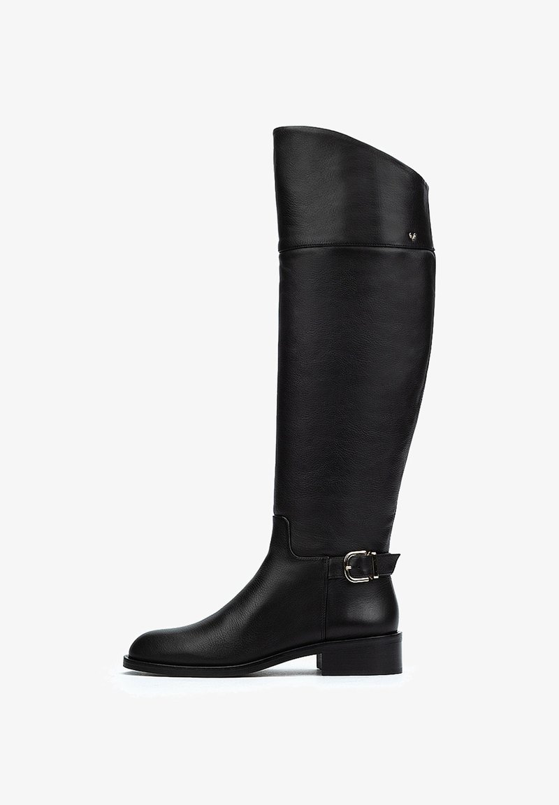 Bota de cuero negro hasta la rodilla con textura suave, punta redondeada, tacón bajo y detalle de hebilla lateral. Diseño único del eje alto.