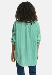 Camisetta a righe verdi e bianche con maniche arrotolate, orlo arrotondato e dettaglio di piega sulla schiena, realizzata in un tessuto leggero.