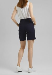 Pantalones cortos ajustados de color azul marino con un frente plano y bolsillos laterales, fabricados con una tela suave y ligera. Combinados con zapatillas blancas de plataforma.
