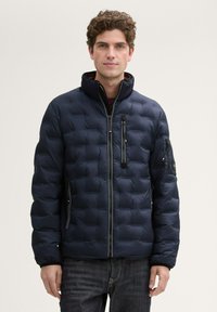 Daunenjacke in Dunkelblau, gesteppter Design mit hohem Kragen und Reißverschluss. Verfügt über seitliche und Ärmel-Reißverschlusstaschen sowie elastische Bündchen.