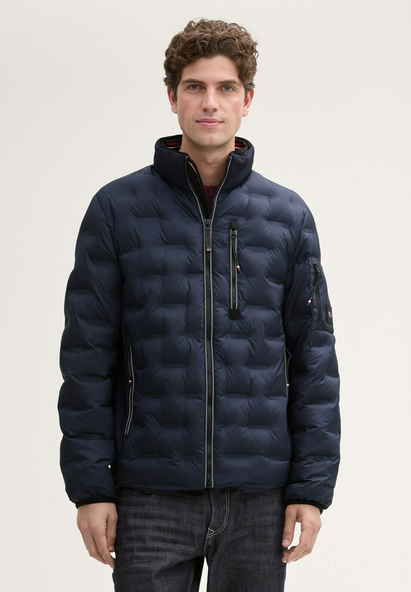 Daunenjacke in Dunkelblau, gesteppter Design mit hohem Kragen und Reißverschluss. Verfügt über seitliche und Ärmel-Reißverschlusstaschen sowie elastische Bündchen.