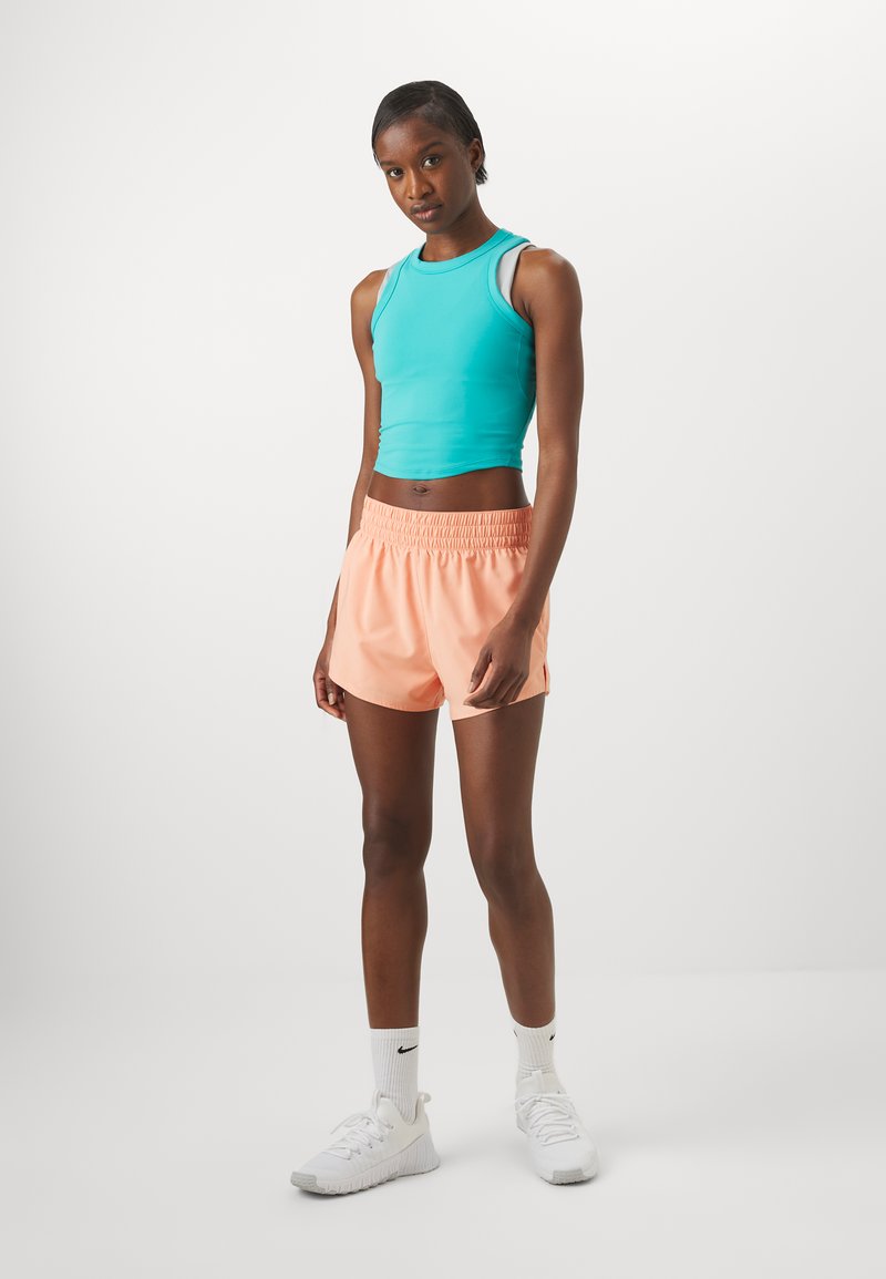 Crop top aqua, shorts pêche avec taille élastique, et chaussures de sport blanches. Texture lisse, design ajusté, et style athlétique.